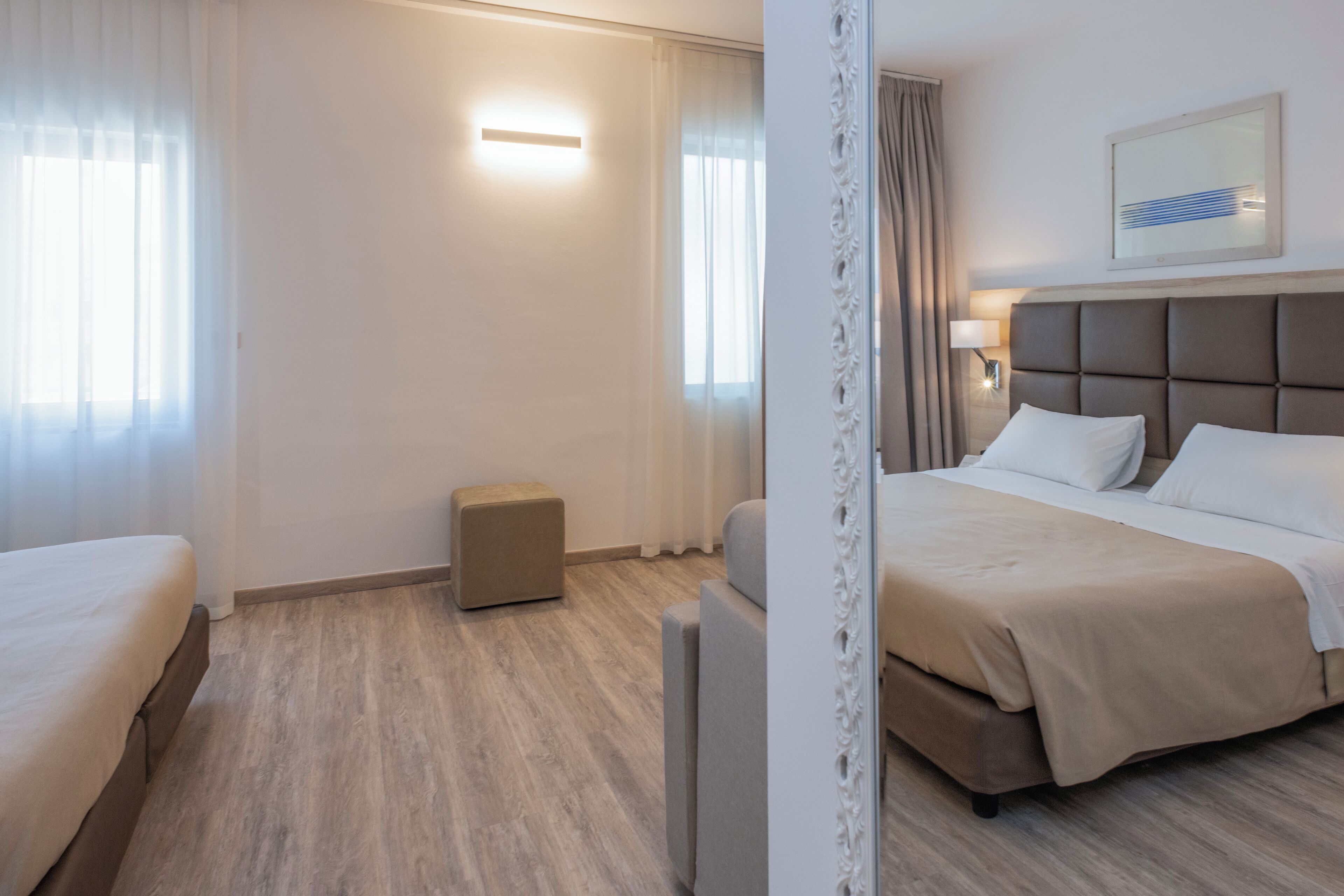 A hotel room with a large bed, a smaller bed, a bedside table, a nightstand, a lamp, and a window with curtains.