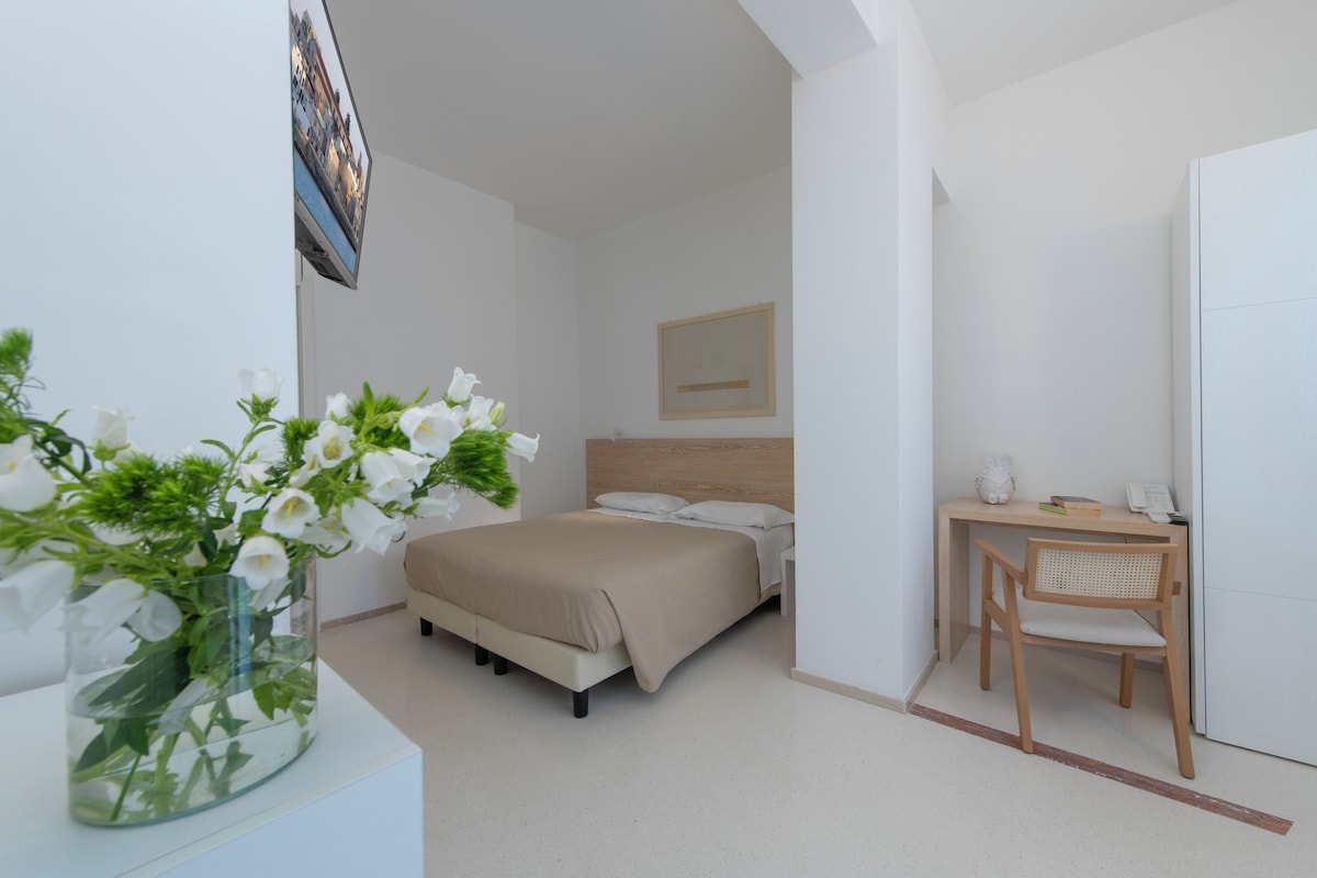 A bedroom with a bed, bedside table, chair, and a desk with a chair.