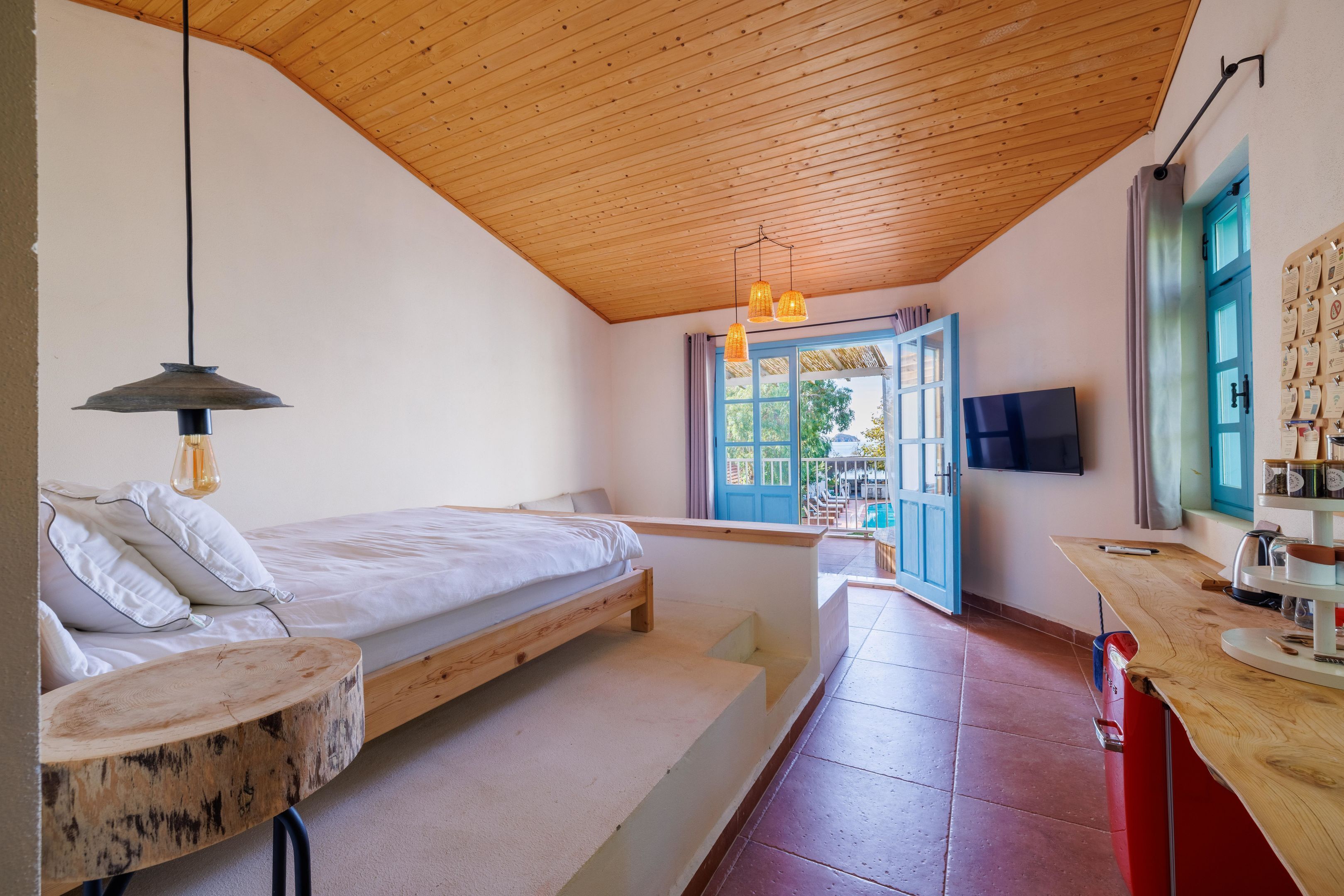 Een slaapkamer met een bed, een houten plafond, een televisie en een raam met gordijnen.