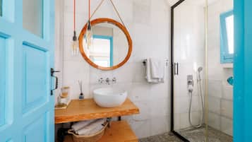 Casa de banho com toucador de madeira, espelho redondo, lavatório branco, chuveiro e porta azul.
