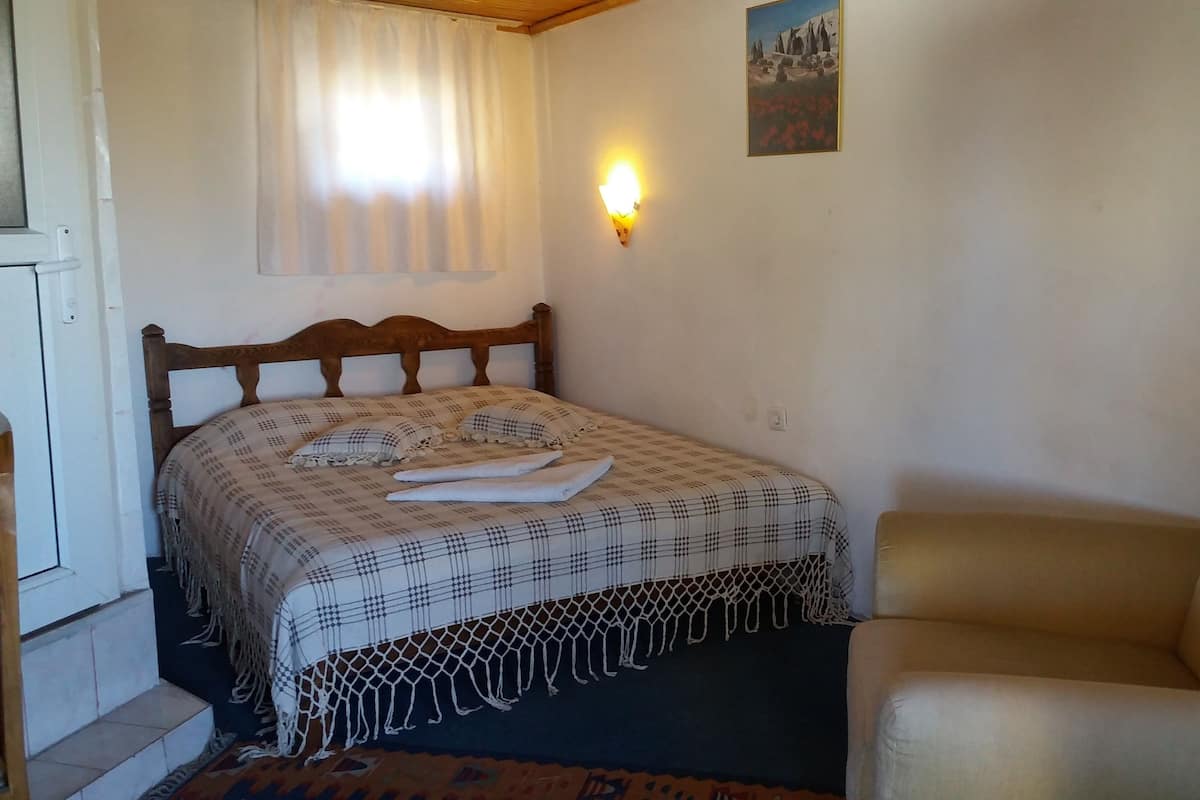 A bedroom with a bed, a chair, a wall-mounted light, and a painting.