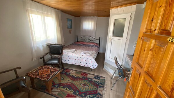 A small, cozy room with a bed, a chair, a table, and a wooden door with a number.