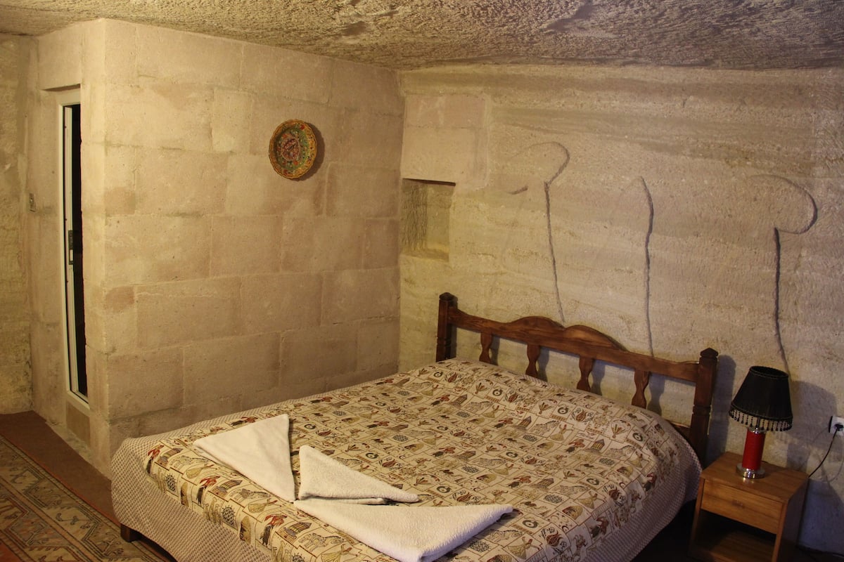 A bedroom with a bed, a wooden nightstand, a lamp, and a patterned bedspread.
