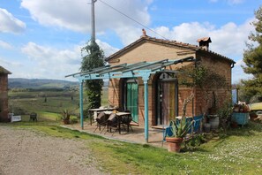 A rustic brick house with a covered patio, a table and chairs, and potted plants. - Bioagriturismo Podere Pretoia (San Gimignano)