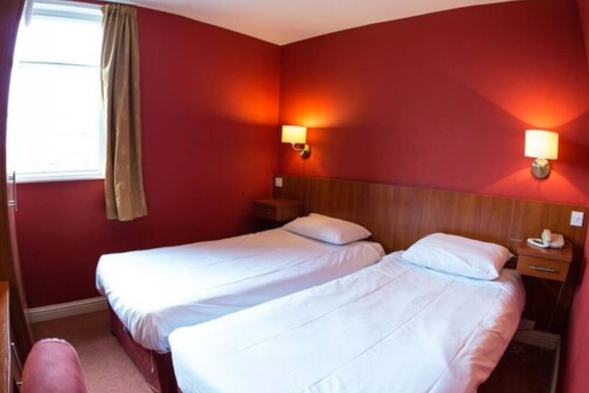 A hotel room with two single beds, a wooden headboard, bedside lamps, a nightstand with a phone, and a window with curtains.