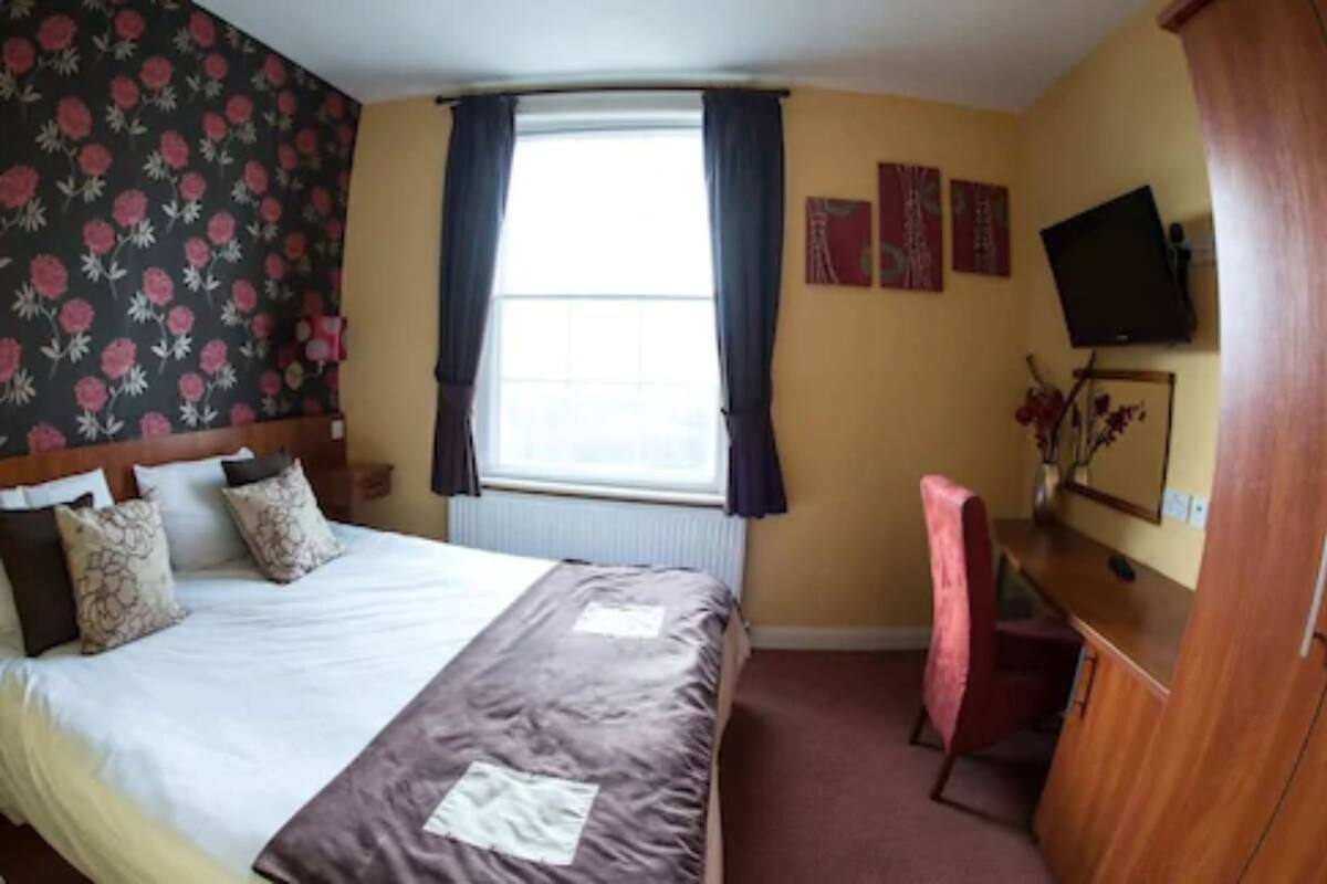 A hotel room with a bed, a desk, a chair, a TV, and a window with curtains.