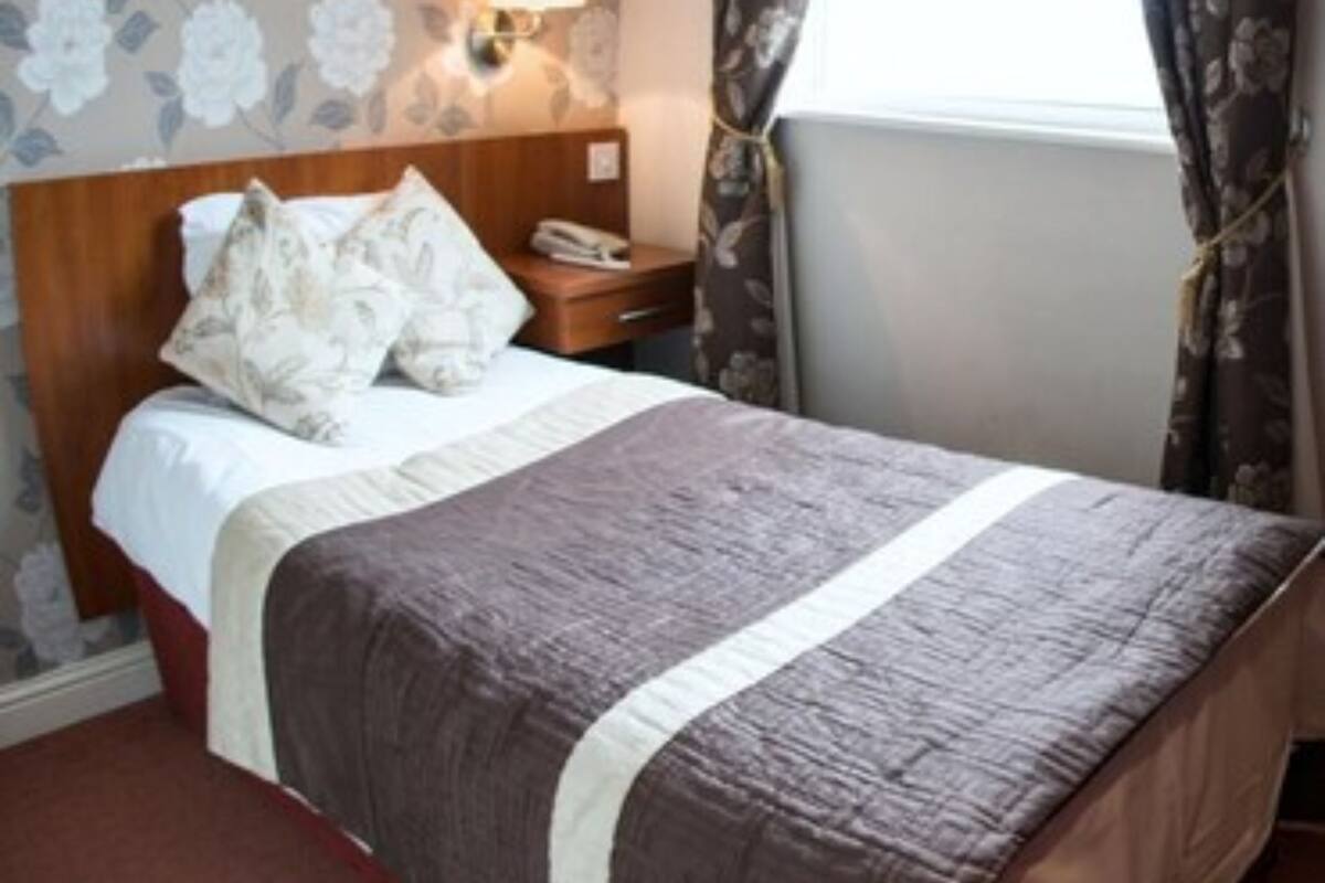 A hotel room with a bed, a nightstand, a lamp, and a window with curtains.
