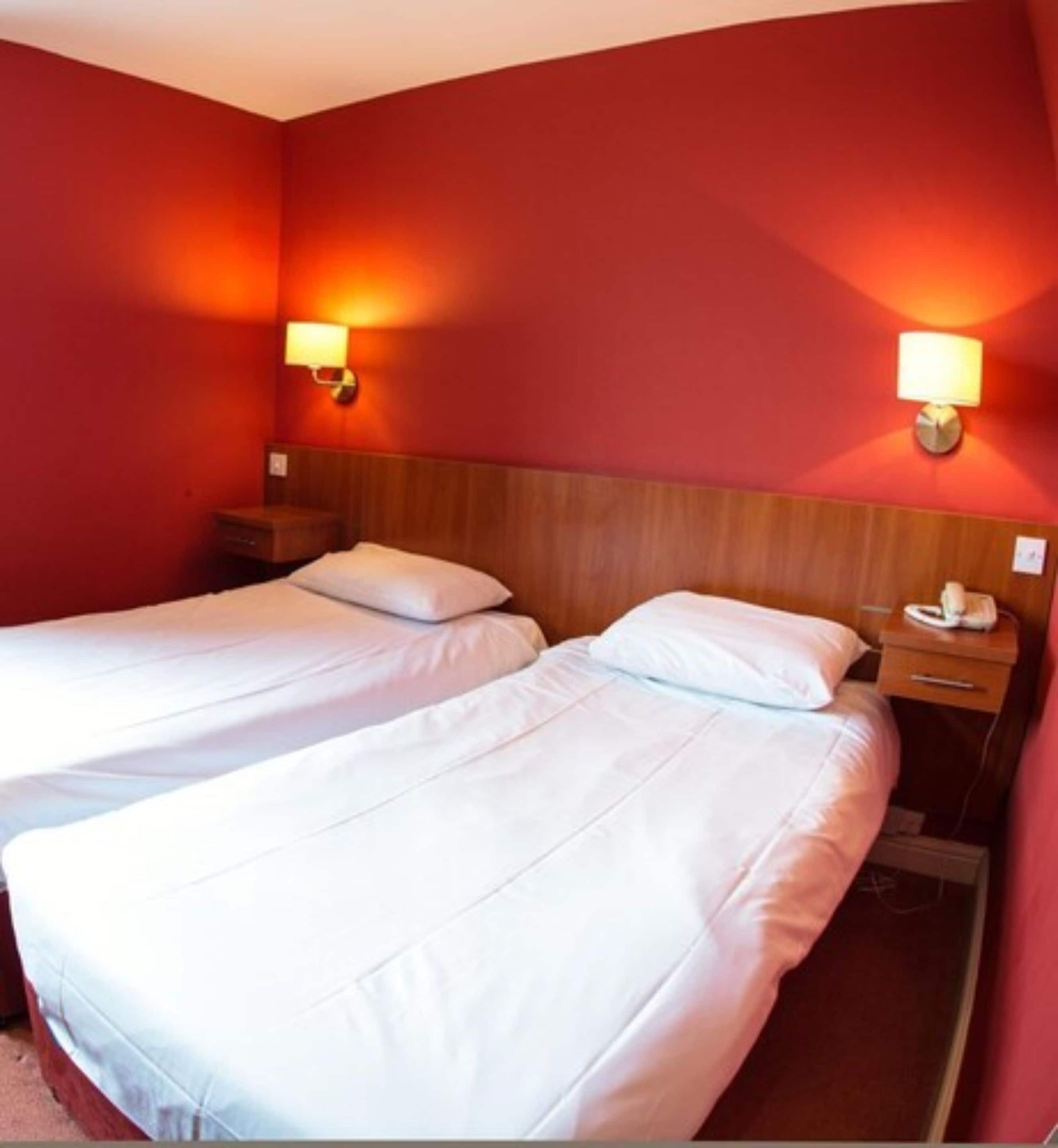 Una habitación de hotel con dos camas individuales, cabeceros de madera y lámparas de noche.