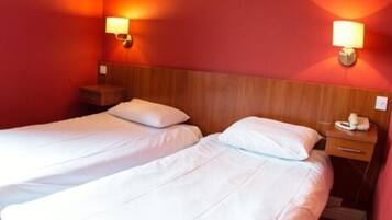 Una habitación de hotel con dos camas individuales, cabeceros de madera y lámparas de noche.