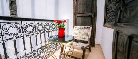 A balcony with a glass table, a red vase with flowers, a white chair, and ornate metal railings.