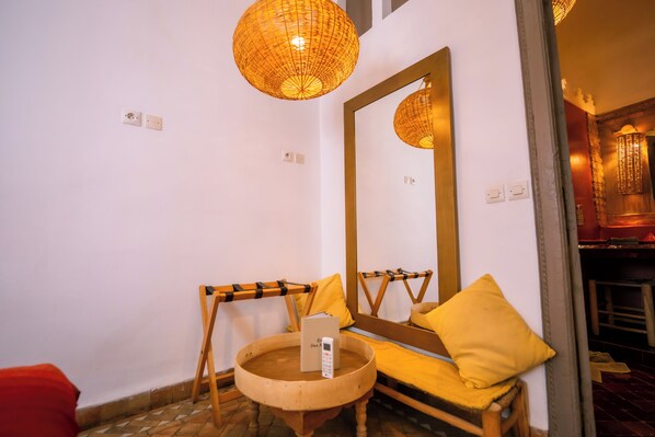 A bathroom with a large mirror, a wooden chair, a small round table with a remote control, and a yellow pillow. - Riad Dar Massai (Marrakech)