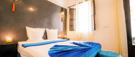 A hotel room with a bed, bedside tables, and a window with curtains.