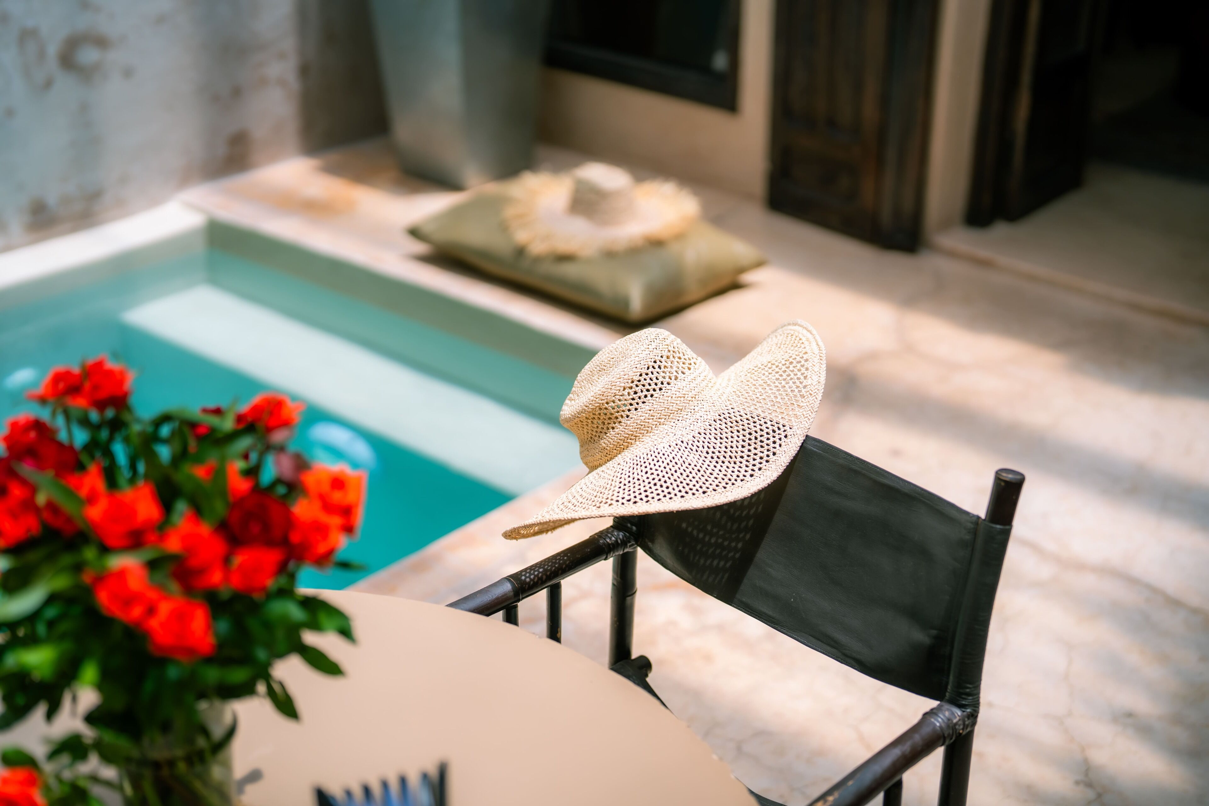 A chair with a woven hat, a pool, and red flowers.