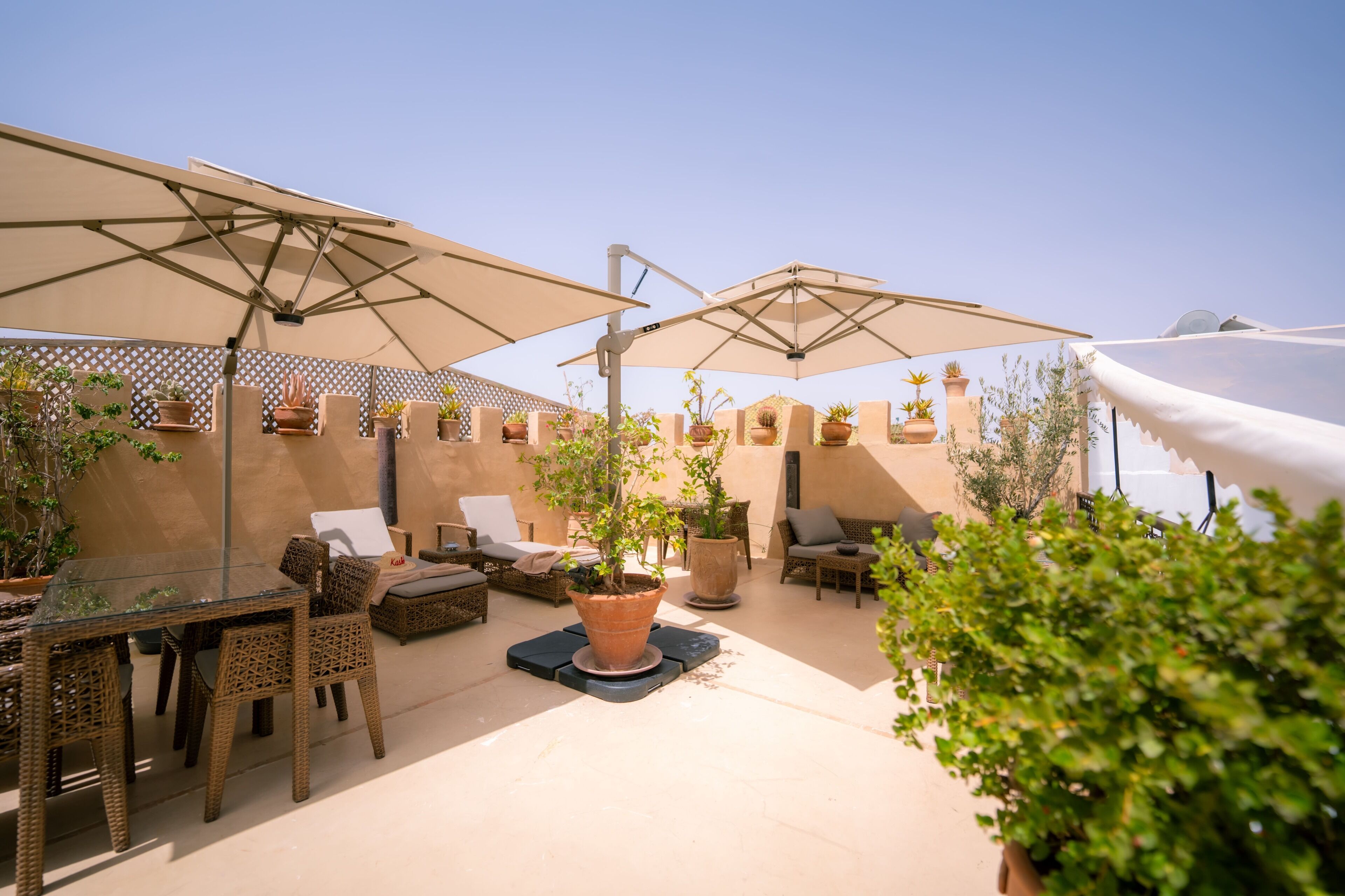 An outdoor patio area with a glass table, wicker chairs, and potted plants.