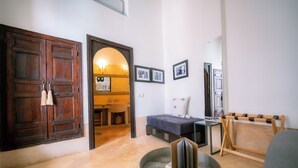 A room with a wooden door, a sofa, a small table, and a mirror. - Riad Dar Massai (Marrakech)