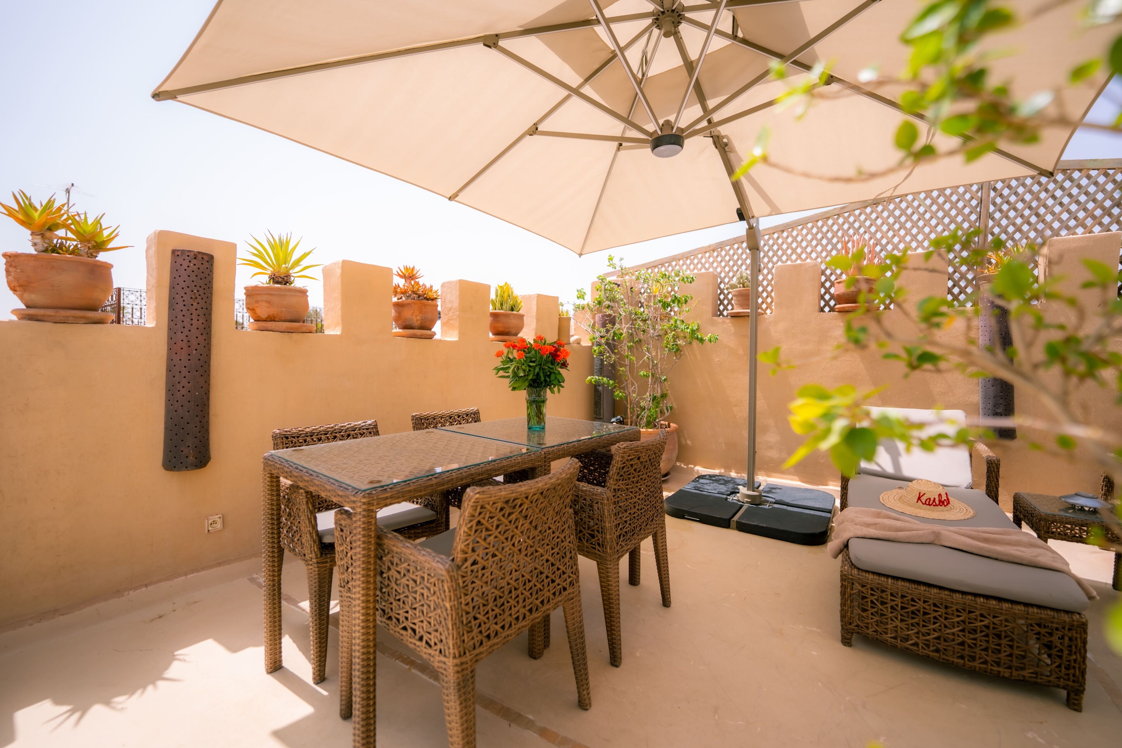 An outdoor patio with a glass table, wicker chairs, a cushioned sofa, and potted plants.