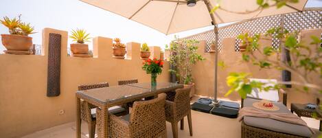 An outdoor patio with a glass table, wicker chairs, a cushioned sofa, and potted plants.
