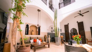 A spacious indoor area with a high ceiling, featuring a wooden coffee table, a potted plant, and a large cactus. - Riad Dar Massai (Marrakech)