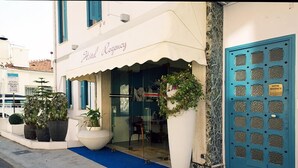 Una entrada de hotel con una puerta azul, una planta grande en maceta y una alfombra azul que conduce a la entrada.