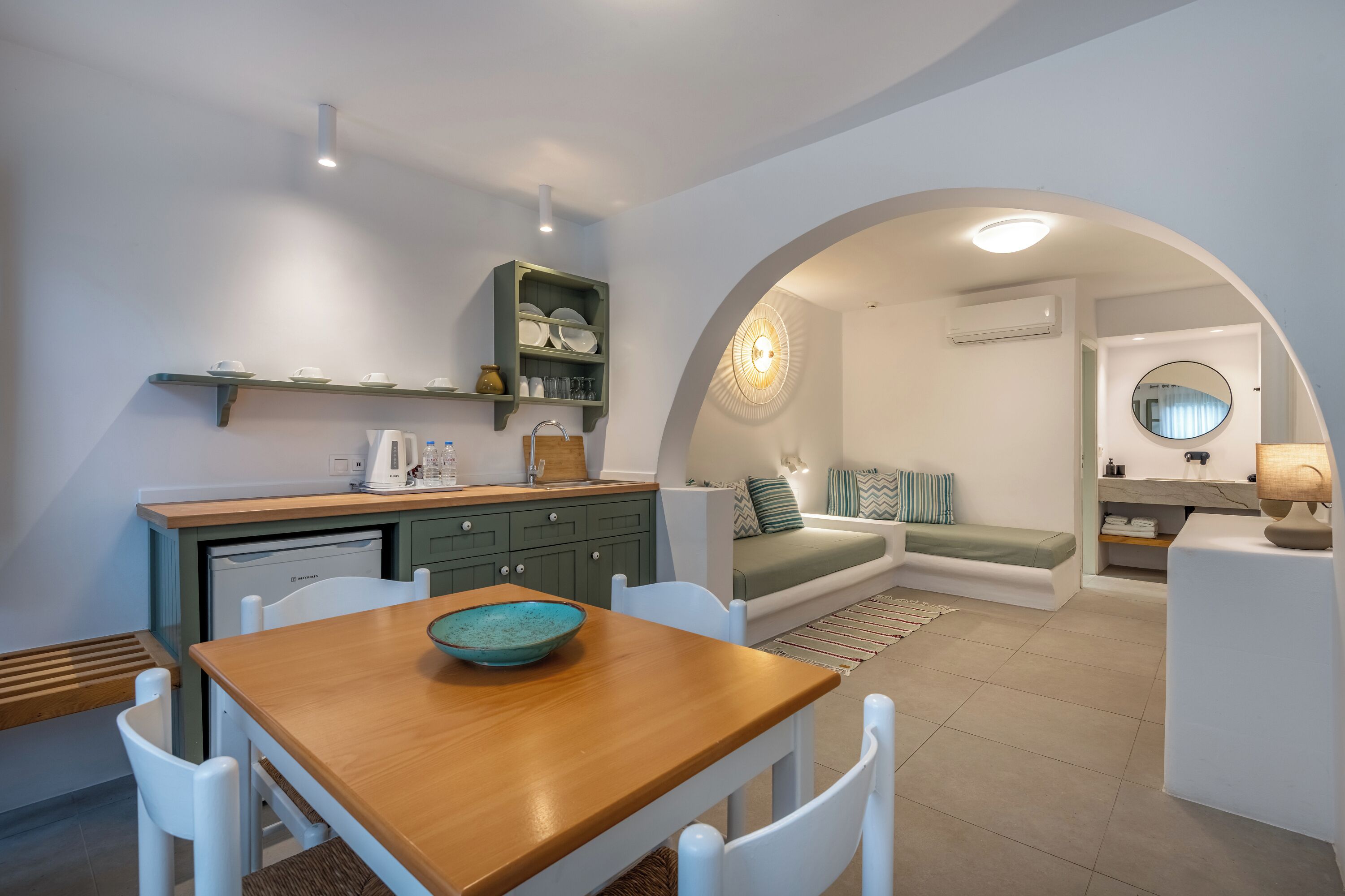 A compact living space with a kitchenette, dining area, and a cozy seating area with a sofa and a round mirror.
