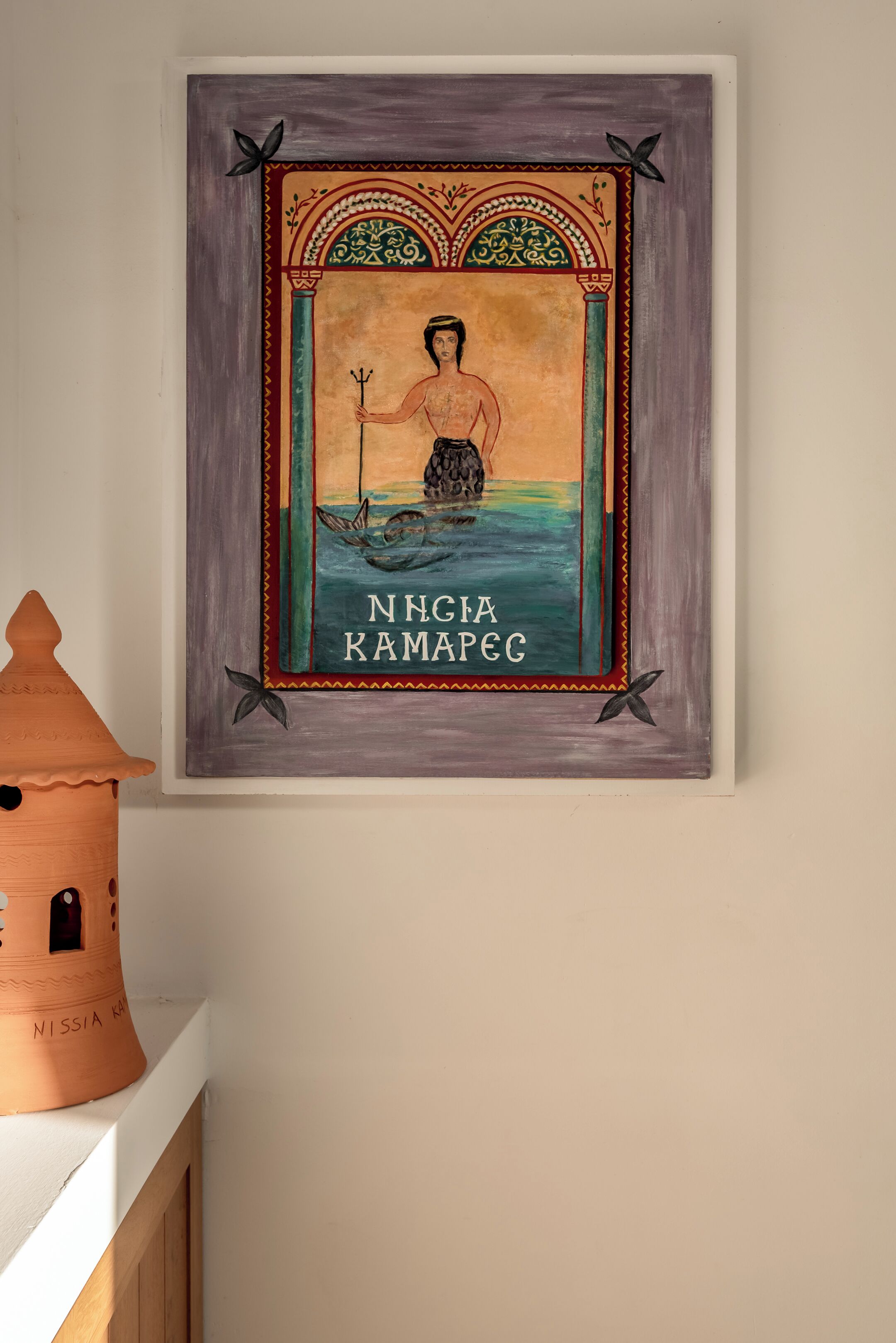 Een ingelijste afbeelding met een figuur, een boot en de tekst 'NNGIA KAMAPEG' aan een muur.