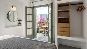 A bedroom with a bed, a wardrobe, a mirror, and an open door leading to a balcony with a table and chairs.