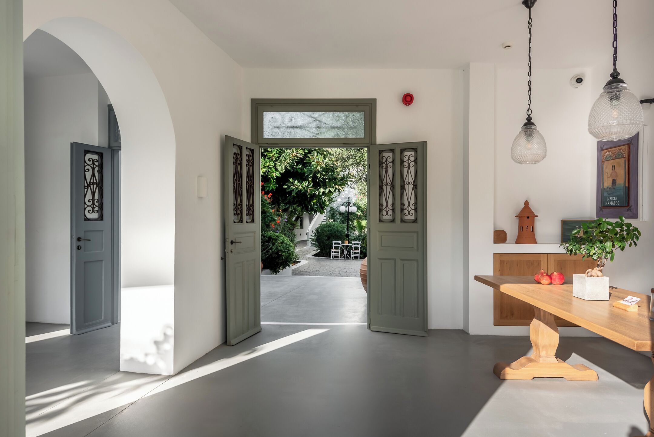 An interior with a hallway leading to an open door, a wooden table with a potted plant, and a hanging light fixture.