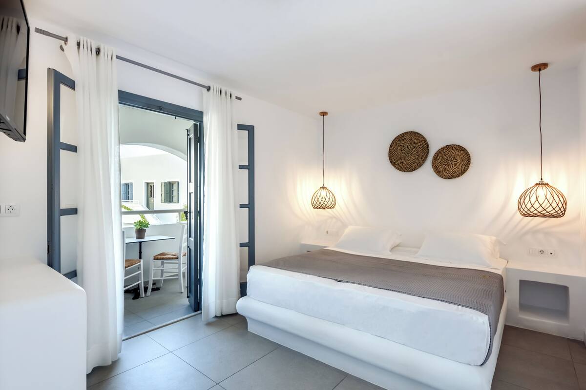 Een slaapkamer met een bed, nachtkastjes, een bureau met stoel en uitzicht door een open deur.