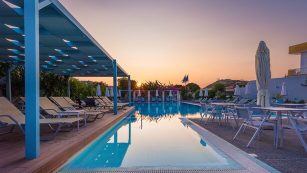 A pool area with lounge chairs and umbrellas, a clear sky, and a sunset.