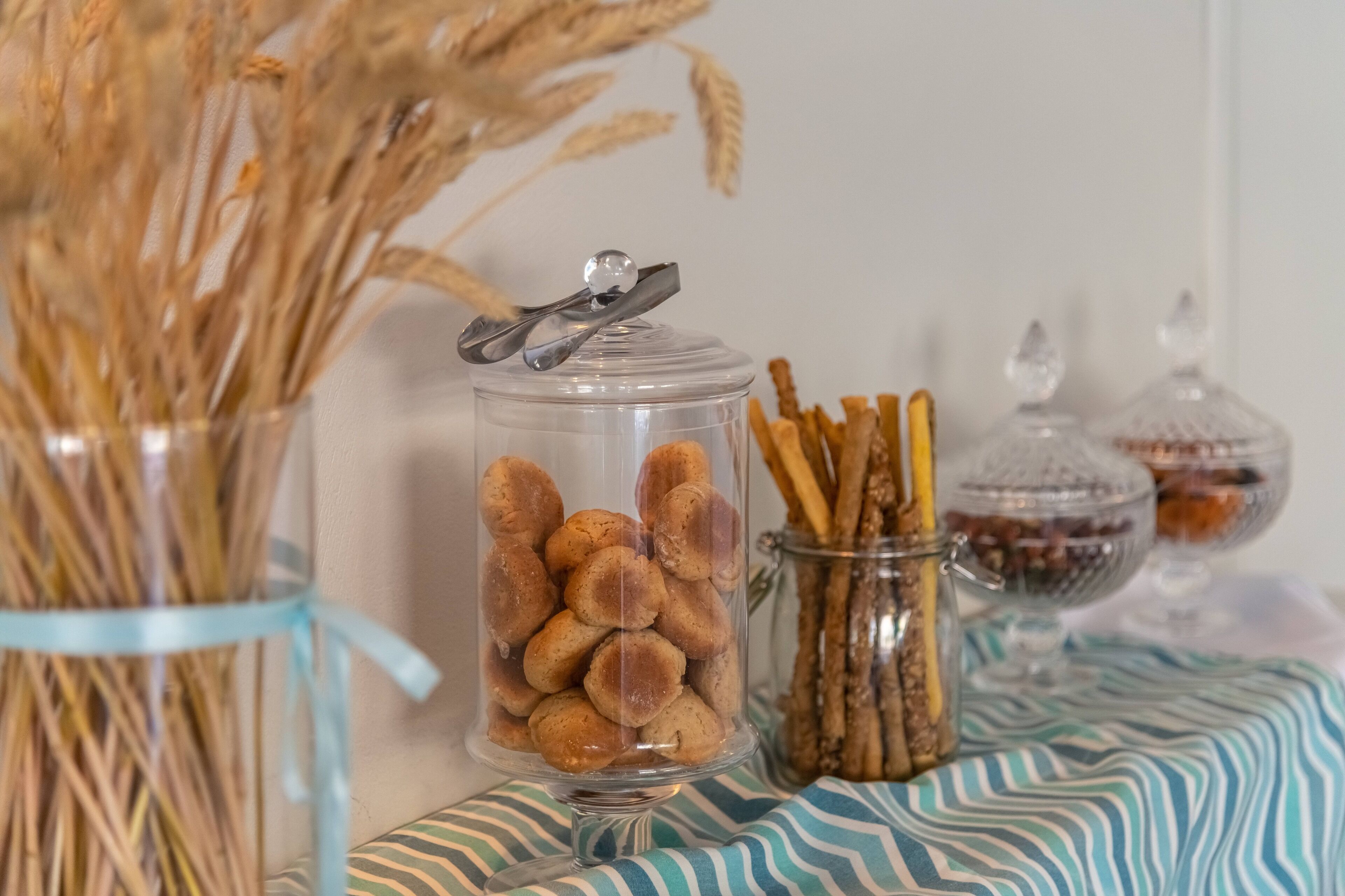 Un bocal en verre rempli de biscuits, un autre contenant des bretzels et un troisième avec des fruits secs, le tout posé sur une nappe à rayures.