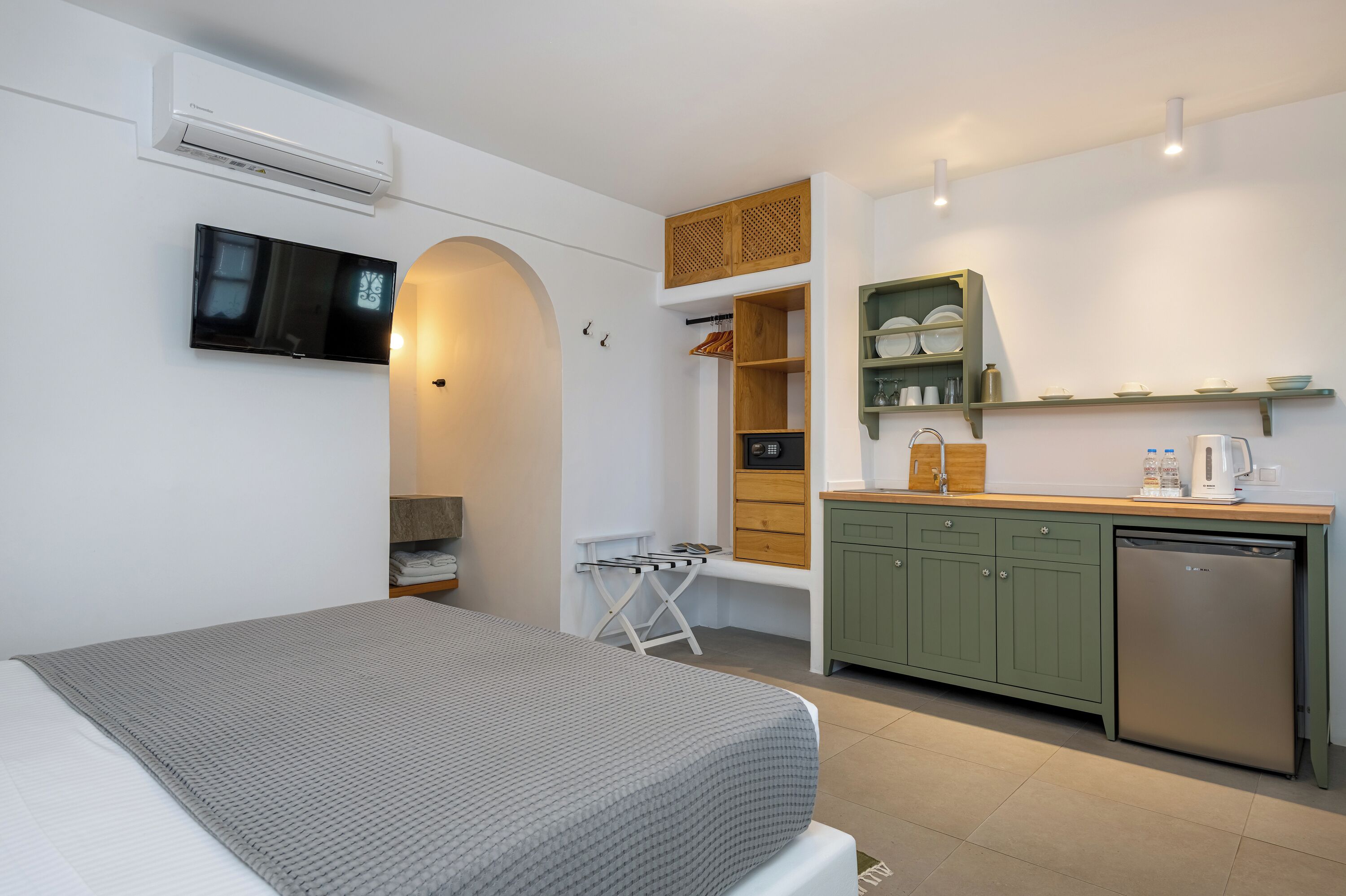 Una habitación compacta con cama, televisión, kitchenette pequeño y lavadora integrada.