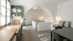 A compact kitchen with a wooden countertop, a built-in shelf with dishes, and a small dining area with a table and chairs.