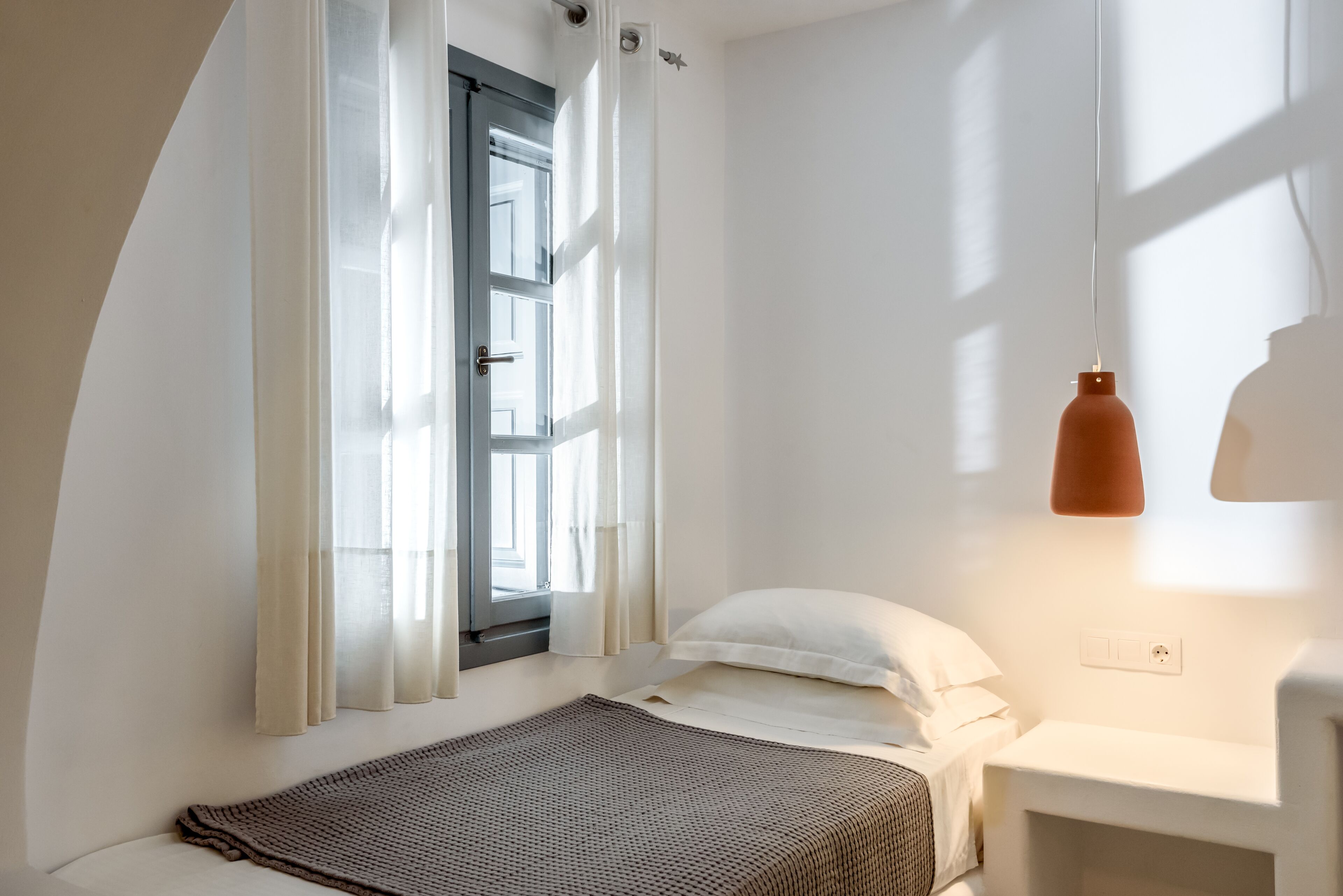 A bedroom with a bed, a window with curtains, a bedside table, and a hanging light fixture.