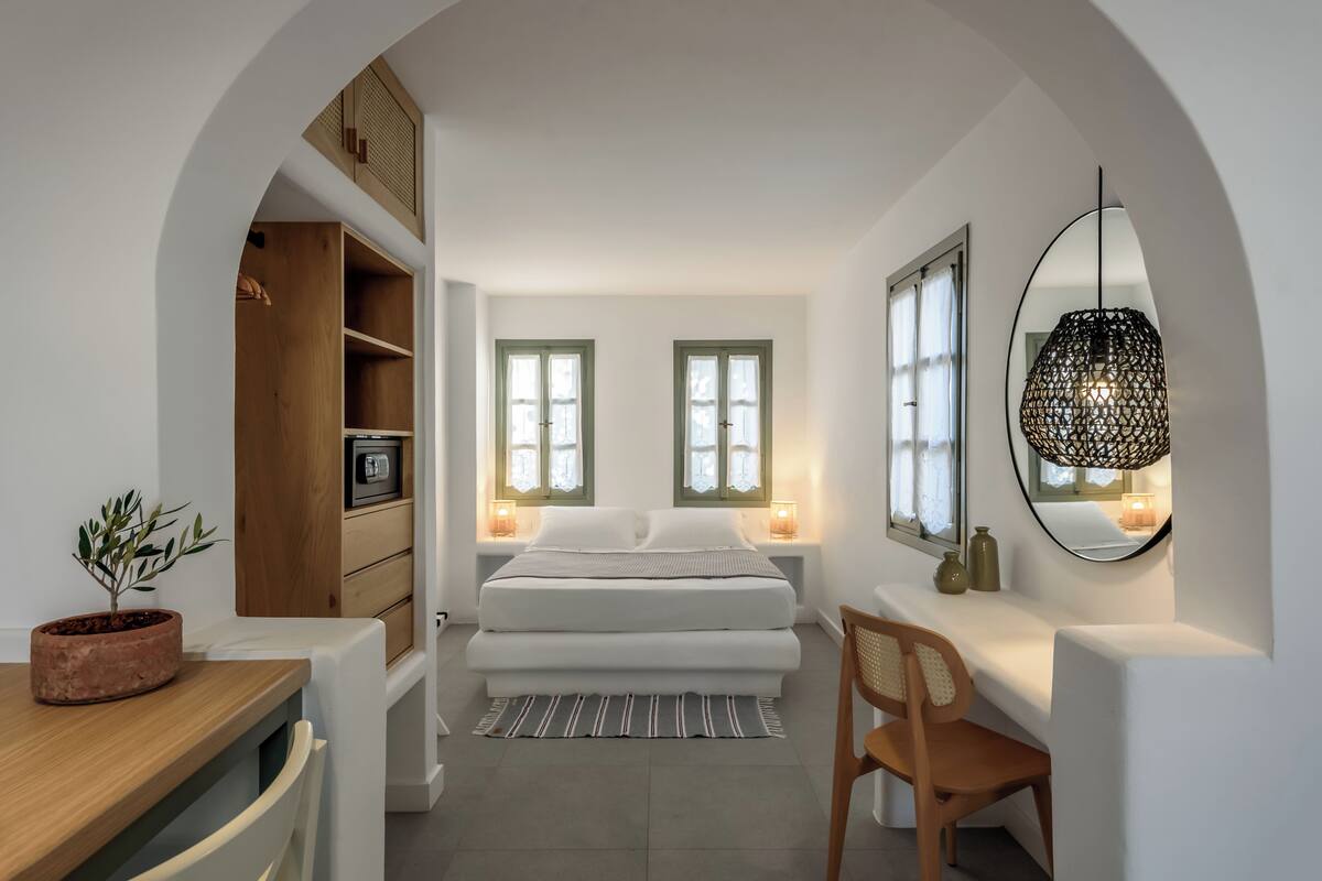 Een slaapkamer met een bed, nachtkastjes, een bureau, een stoel, een potplant en een spiegel.