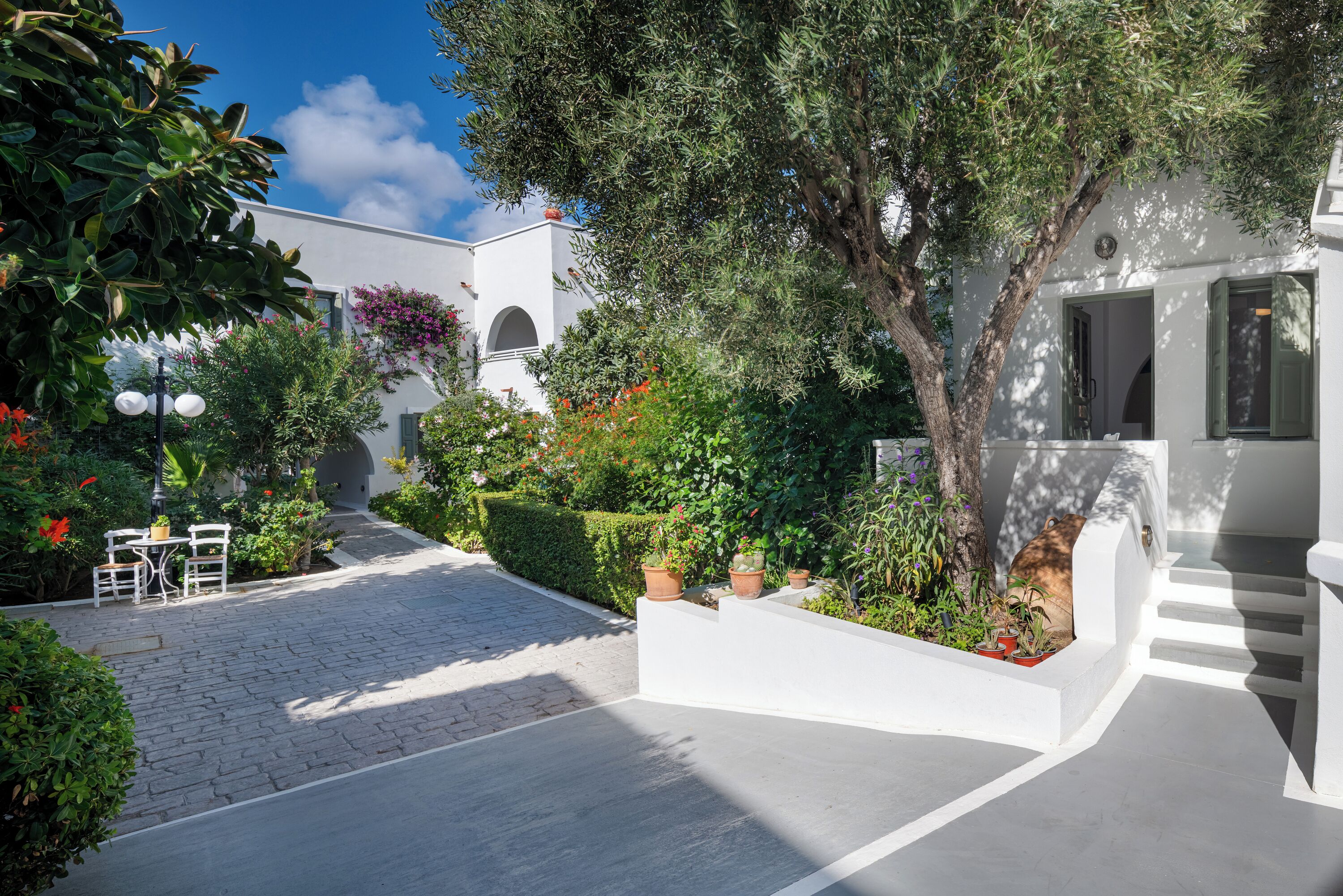 A courtyard with a white building, potted plants, and a table with chairs.