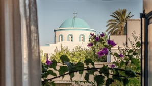 A view of a building with a dome and a cross, surrounded by greenery and flowers.