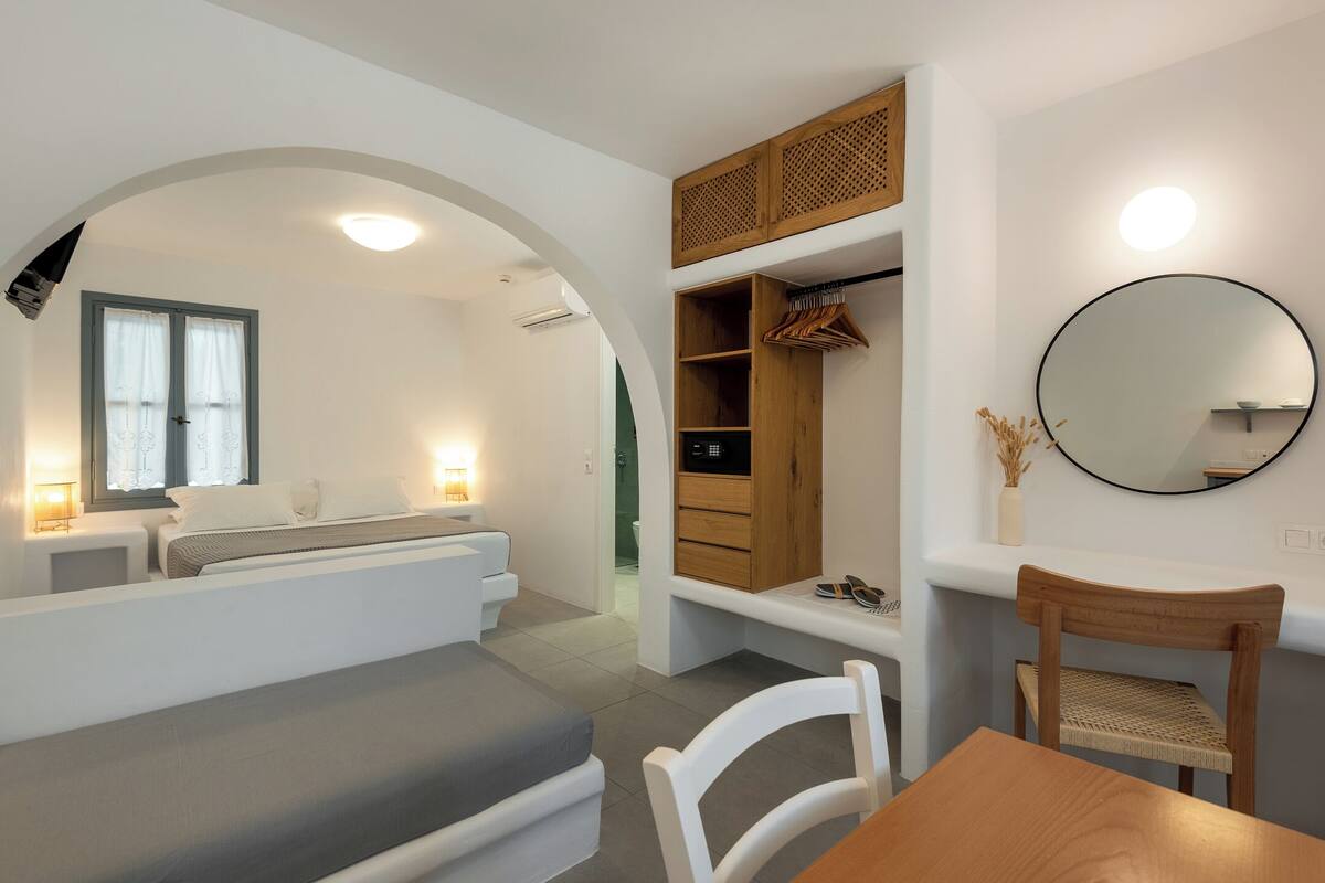 Een moderne kamer met een bed, zithoek, houten kast en een ronde spiegel.