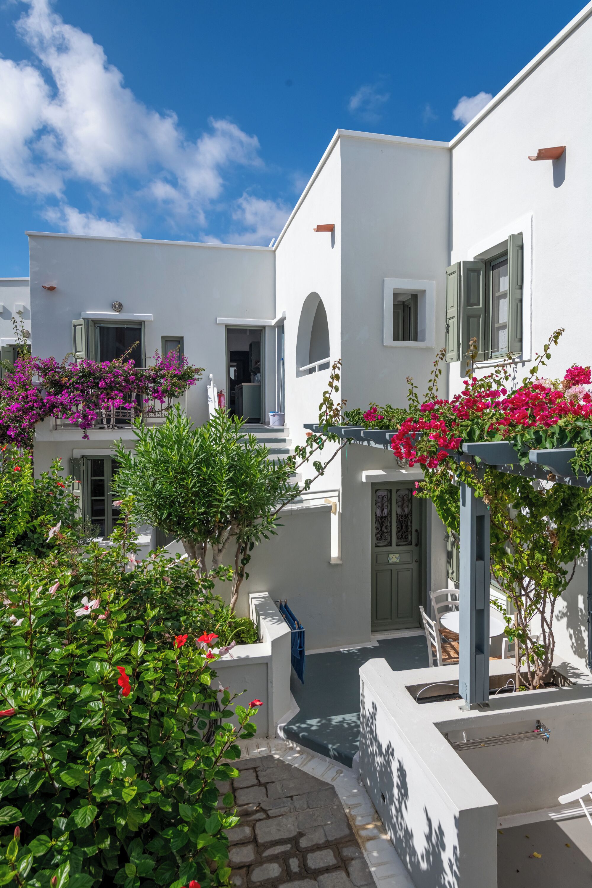 A white building with balconies, a stone pathway, and greenery.