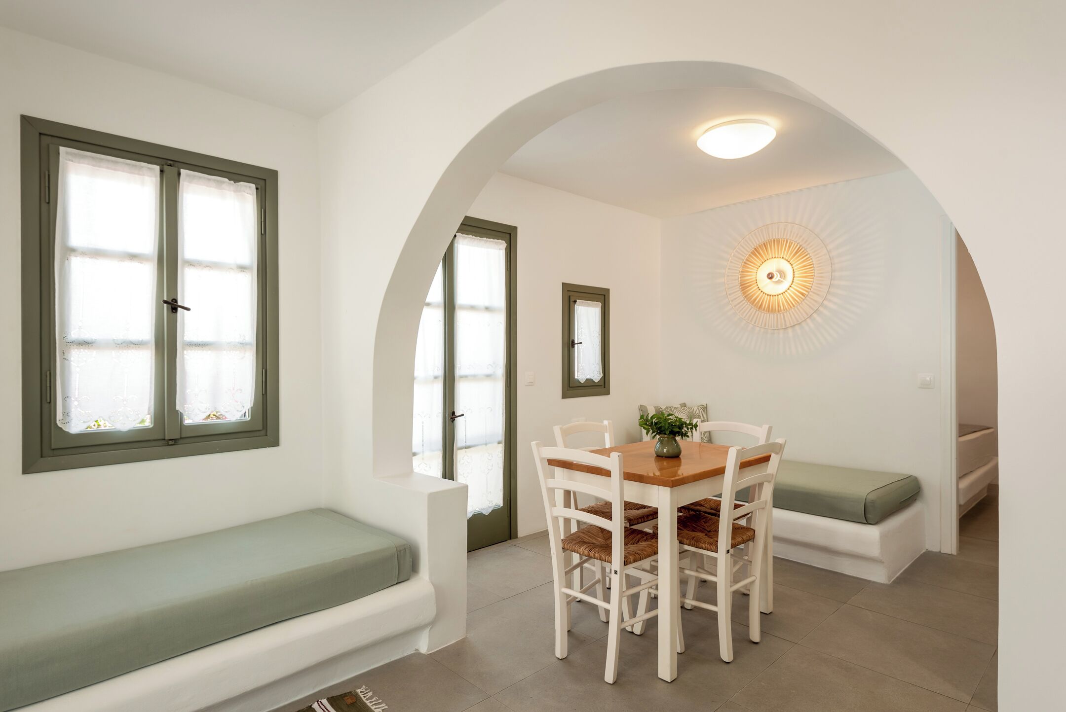 A room with a dining table, chairs, a bench, and a wall-mounted light fixture.