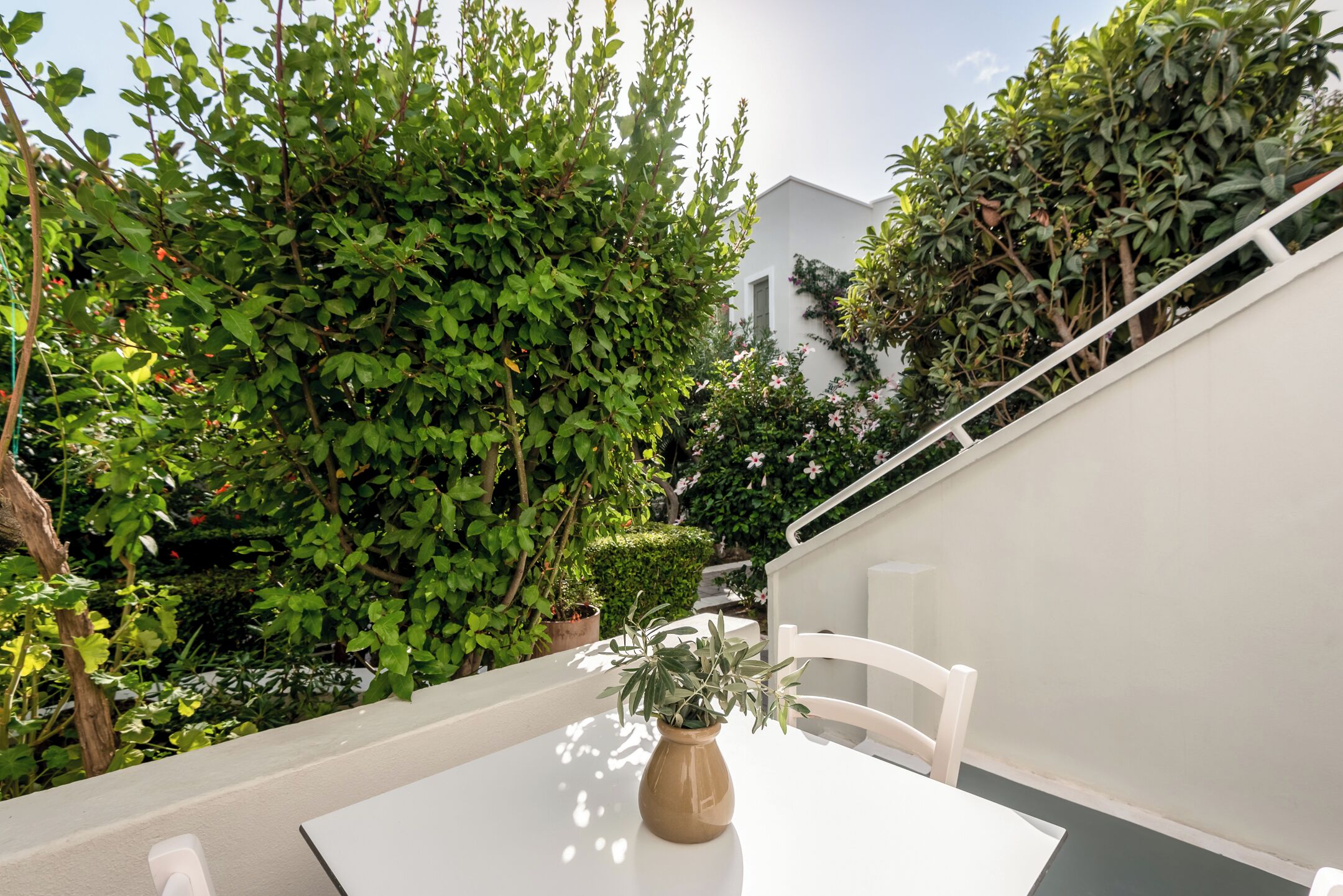 A white table with a vase of green plants, white chairs, and a white railing.