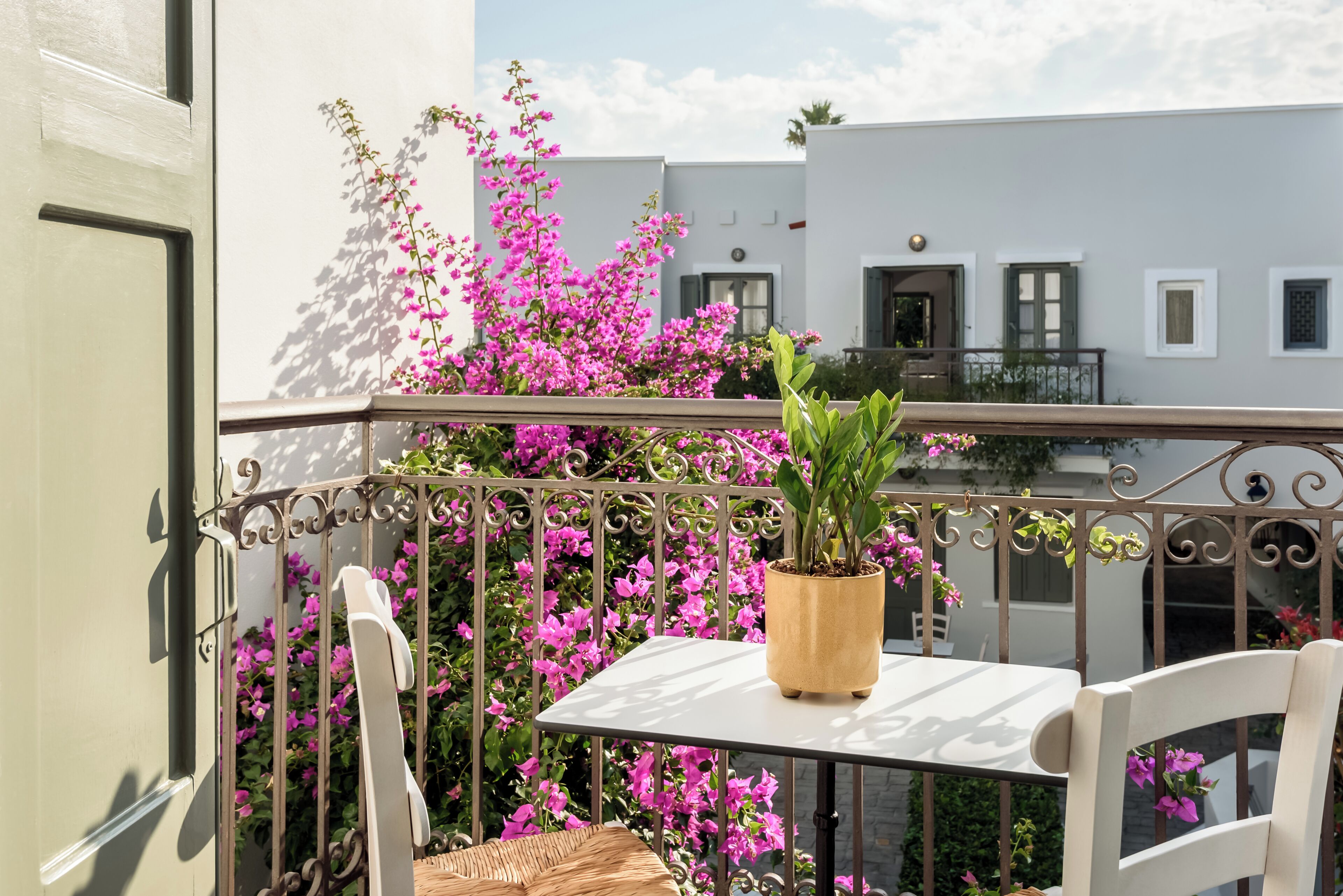 A balcony with a white table, a potted plant, and pink flowers.