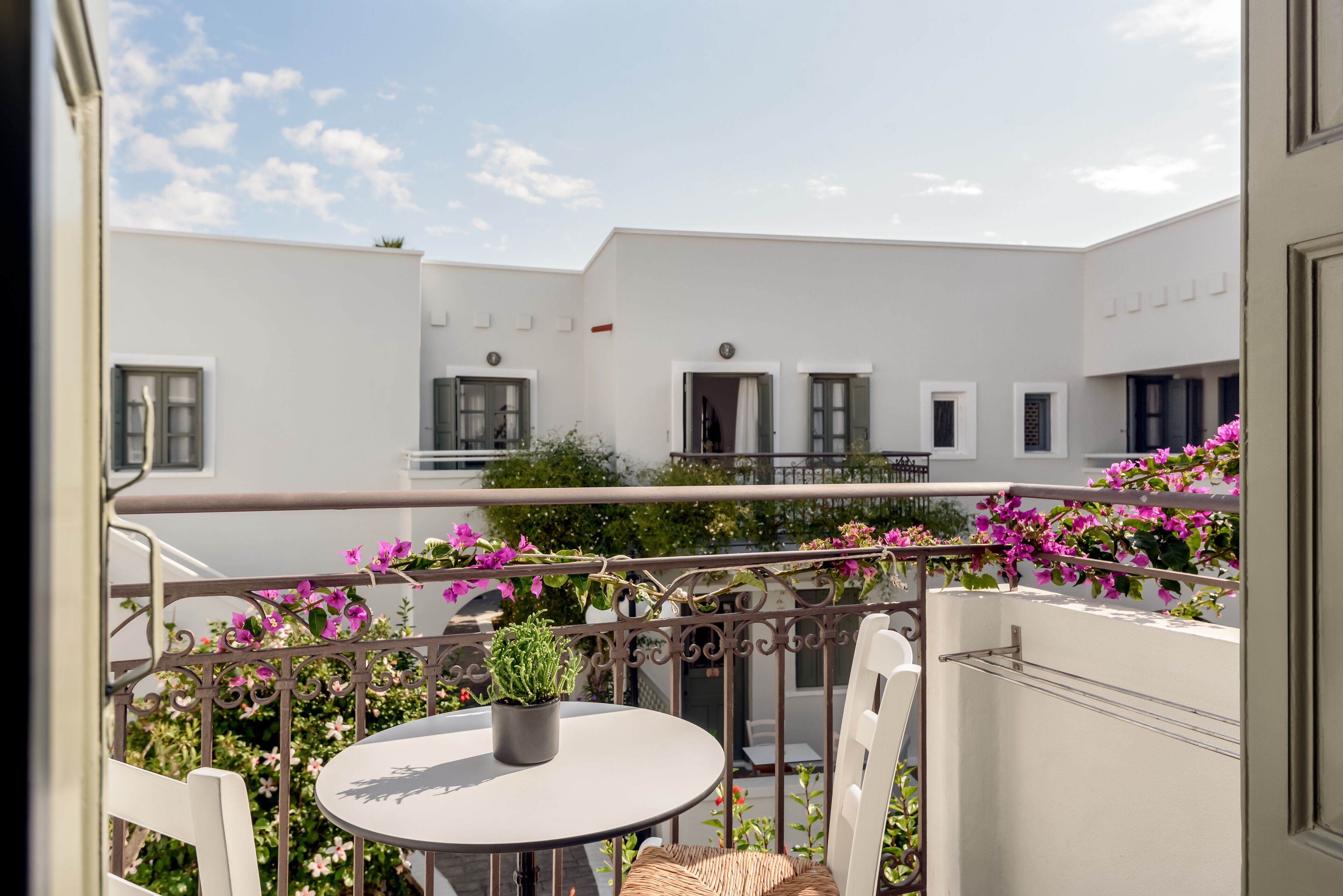 Ein Balkon mit rundem Tisch und Stuhl, umgeben von rosa Blumen und einem Blumentopf.