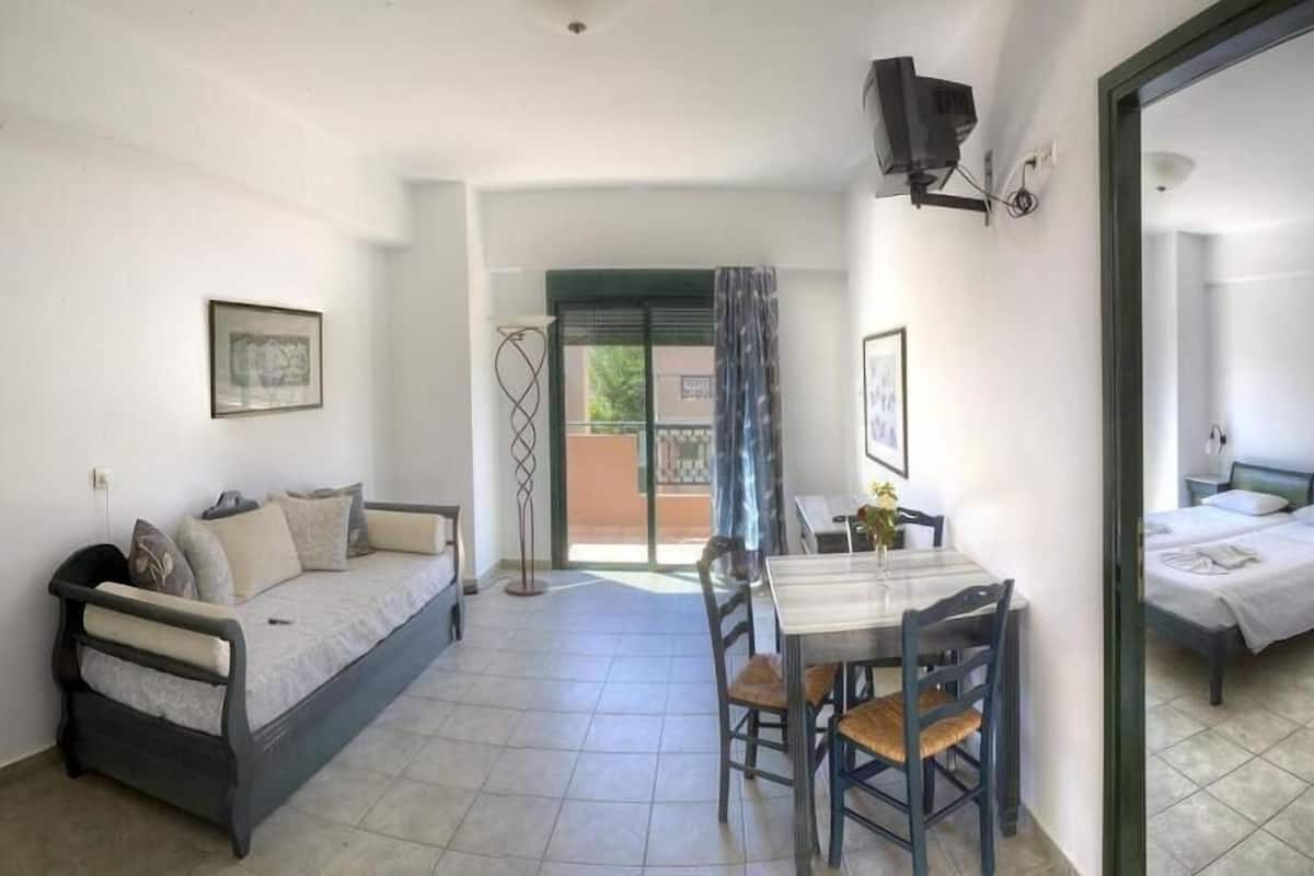 A room with a bed, a sofa, a dining table with chairs, and a TV mounted on the wall.