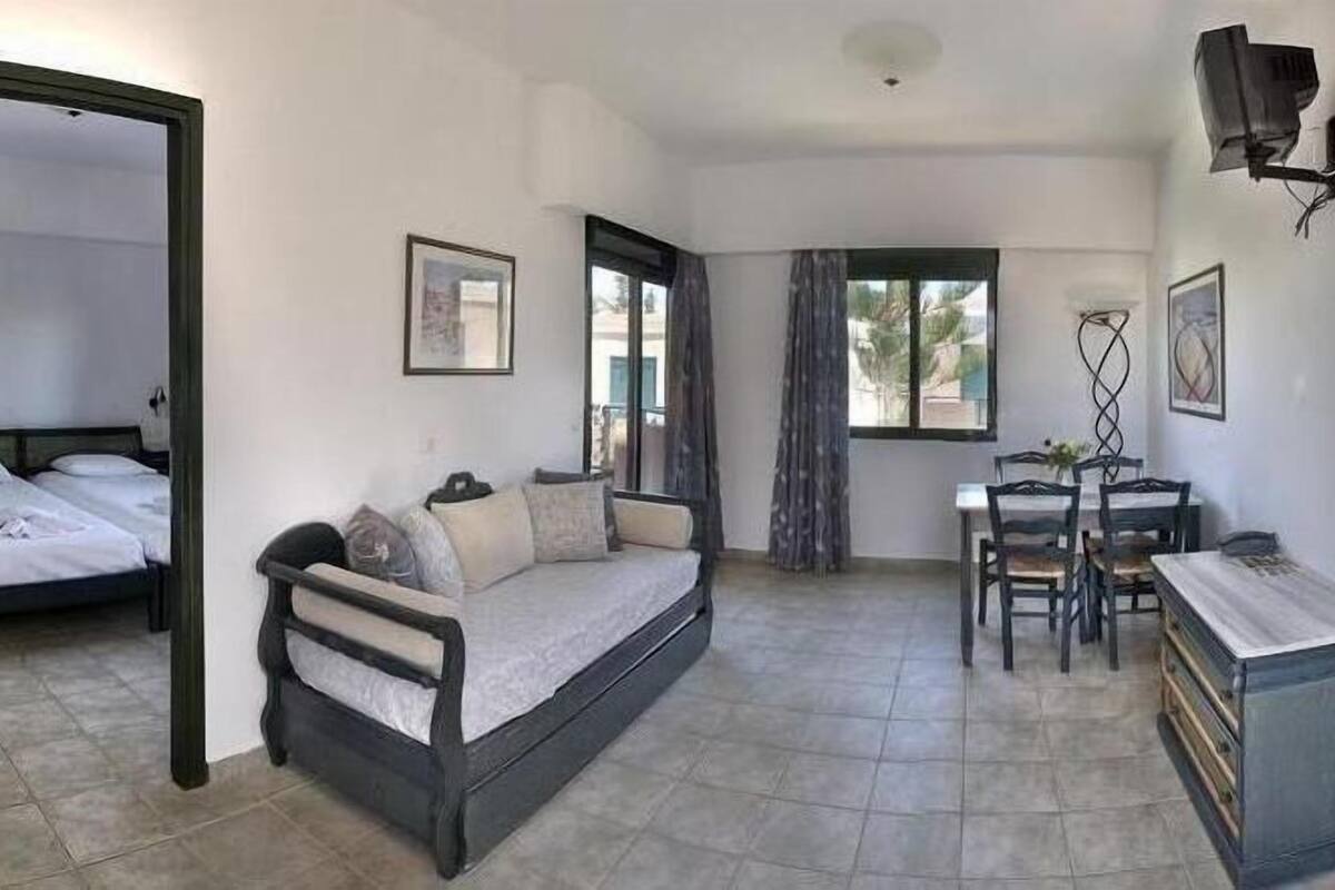 A room with a bed, a sofa, a desk, and a chair. There are windows and a door.