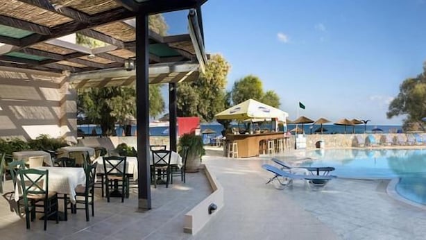 Un área de piscina con sillas de descanso y sombrillas, un bar y asientos al aire libre.