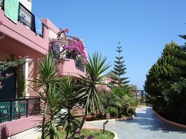 A pathway flanked by lush greenery and a pink building with balconies.