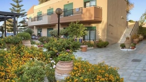 Un edificio de dos pisos con un balcón, rodeado de macetas con plantas y flores.