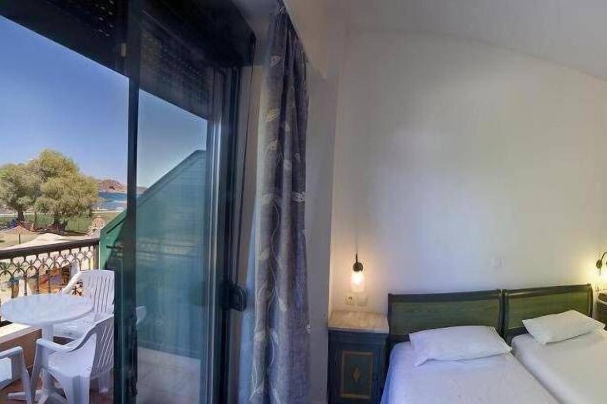 A hotel room with a balcony, a bed, a desk, and a chair.