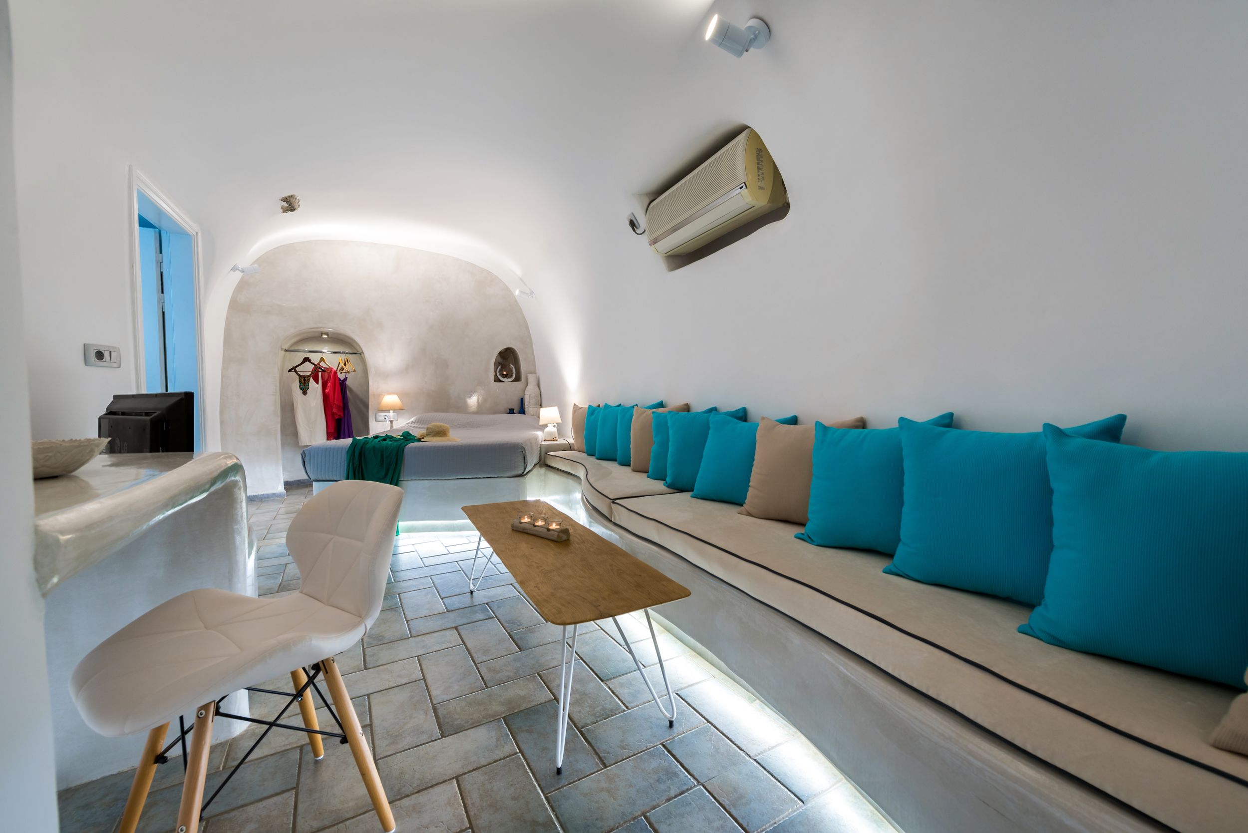 Una sala moderna con un sofá, una mesa de centro y un sillón. Se observa una lámpara colgante y un aire acondicionado instalado en la pared.