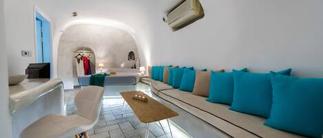 Una sala moderna con un sofá, una mesa de centro y un sillón. Se observa una lámpara colgante y un aire acondicionado instalado en la pared.